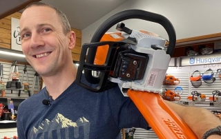 man smiling, holding chainsaw as it sits on his shoulder
