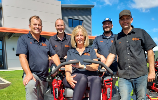Carl's Mower & Saw family gathered around a Gravely mower in front of their new building